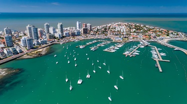 A port city with several sky scrapers and a busy boating area is seen from high above.