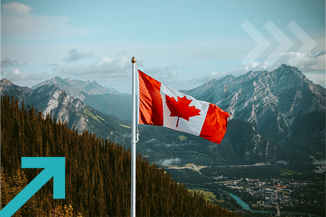 Canadian flag with mountain and small town views in the distance, in the summertime.