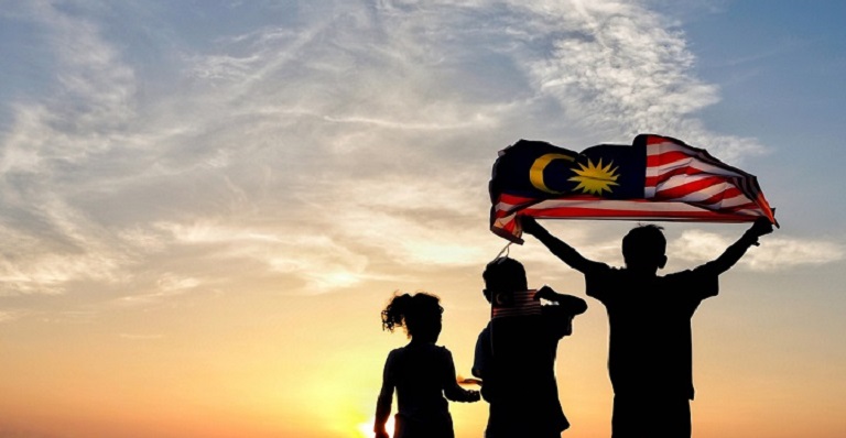 The silhouette of three people against a sunset, one holding the Malaysian flag.