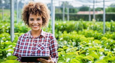 Brazilian female farmer looks at digital tablet with plants in background.