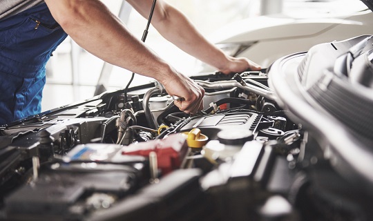 A man’s arms reaching into a car’s engine.