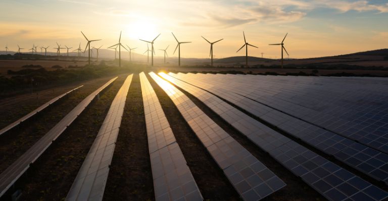 Rangées de panneaux solaires avec des éoliennes en arrière-plan au coucher du soleil.
