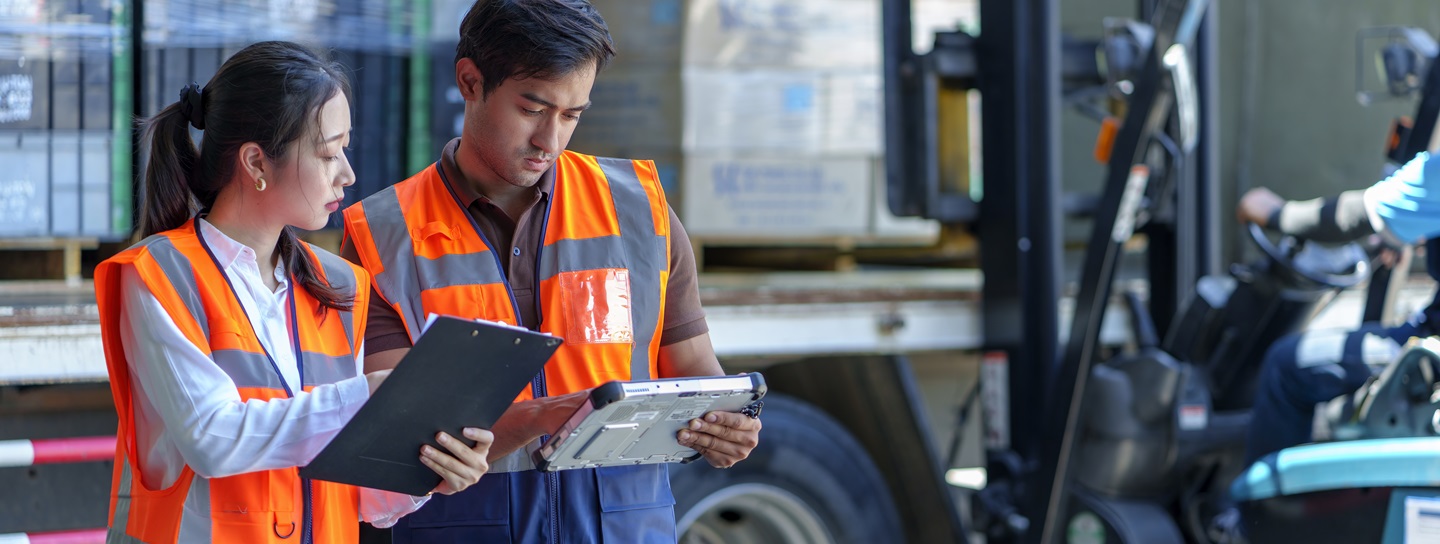 Warehouse workers double-check paperwork as forklift loads shipment into a truck.