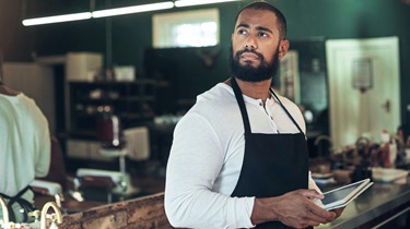 Handsome Black barber looks contemplative while using a digital tablet in his salon