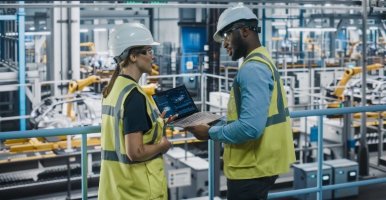 Spécialiste et ingénieure automobile en gilets de sécurité utilisant un portable dans une usine de production.