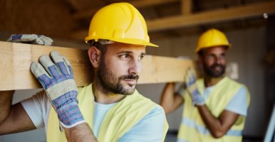 Les ouvriers du bâtiment marchent avec une poutre en bois sur le chantier.