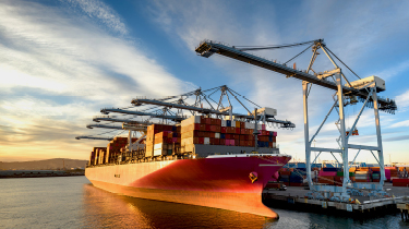 Vue aérienne d’un énorme cargo chargé de conteneurs, à quai dans le port de Long Beach, avec les grues à portique de quai émergeant de la jetée du terminal.