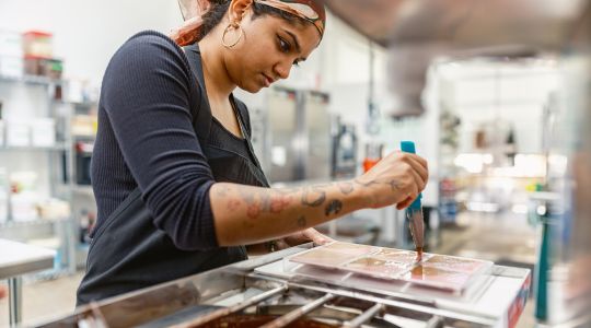 Une chocolatière répartit du chocolat fondu dans un moule à barres à l'intérieur d'une chocolaterie.