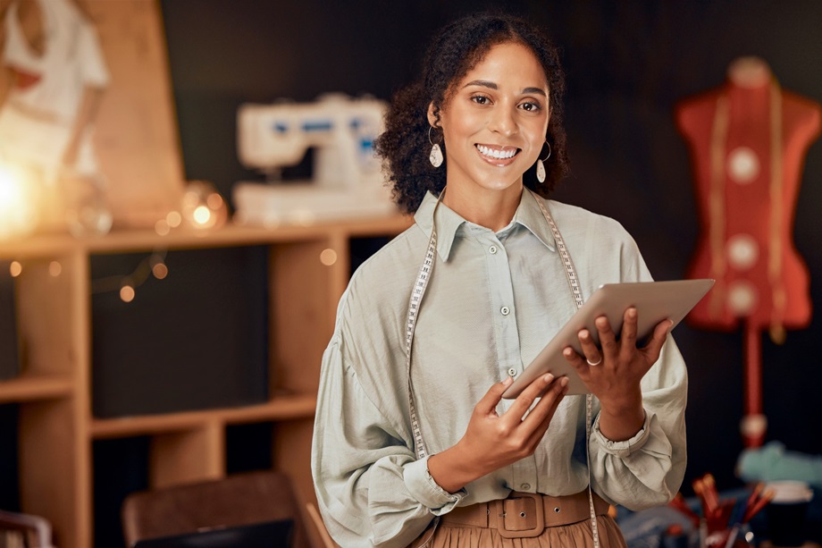 Une femme tenant une tablette sourit à la caméra dans un atelier de couture.