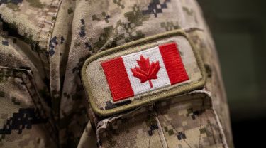 Close-up of a Canadian flag patch sewn onto the sleeve of a camouflage military uniform.