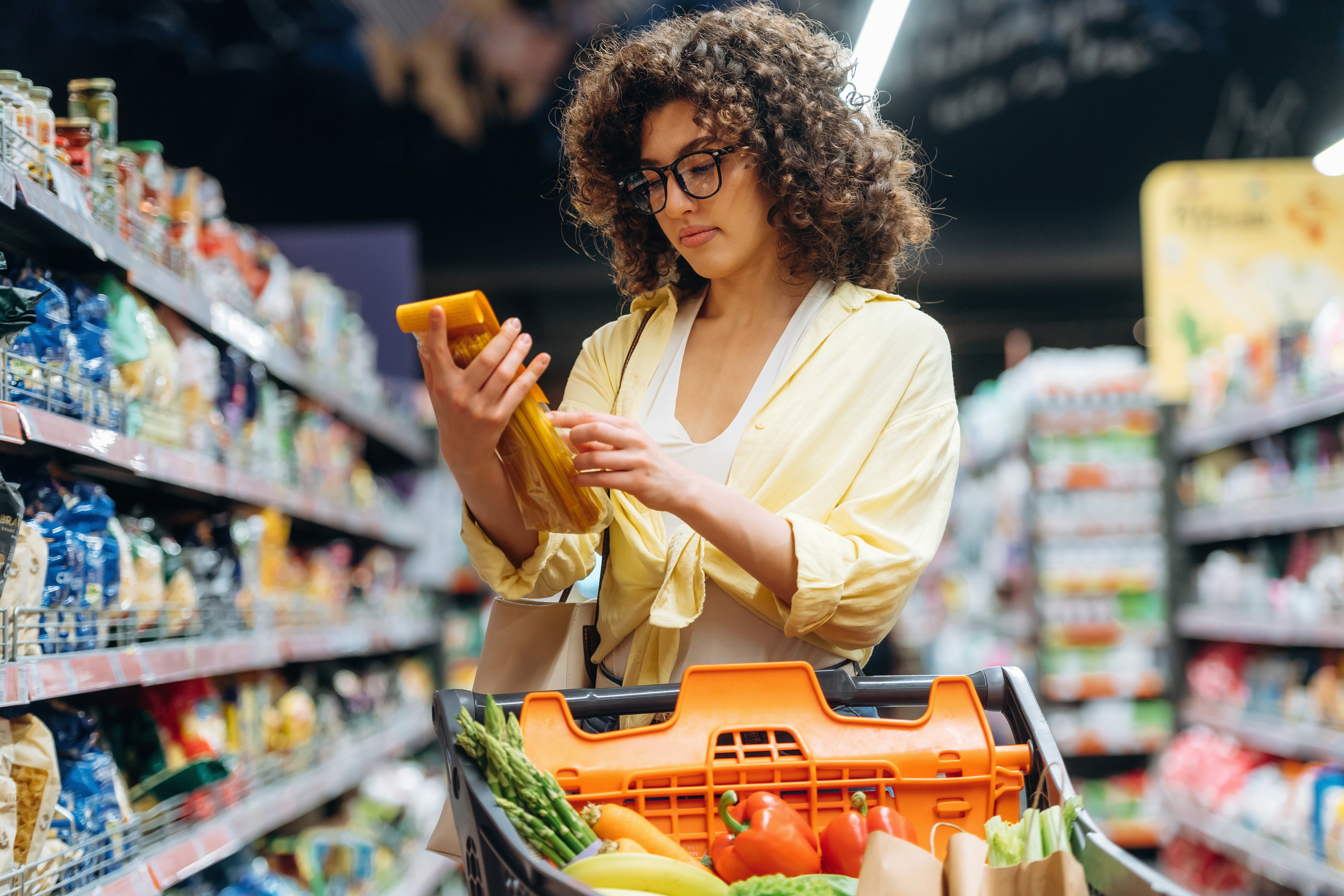 Woman shopping with a cart full of fresh fruits and vegetables in a grocery store.