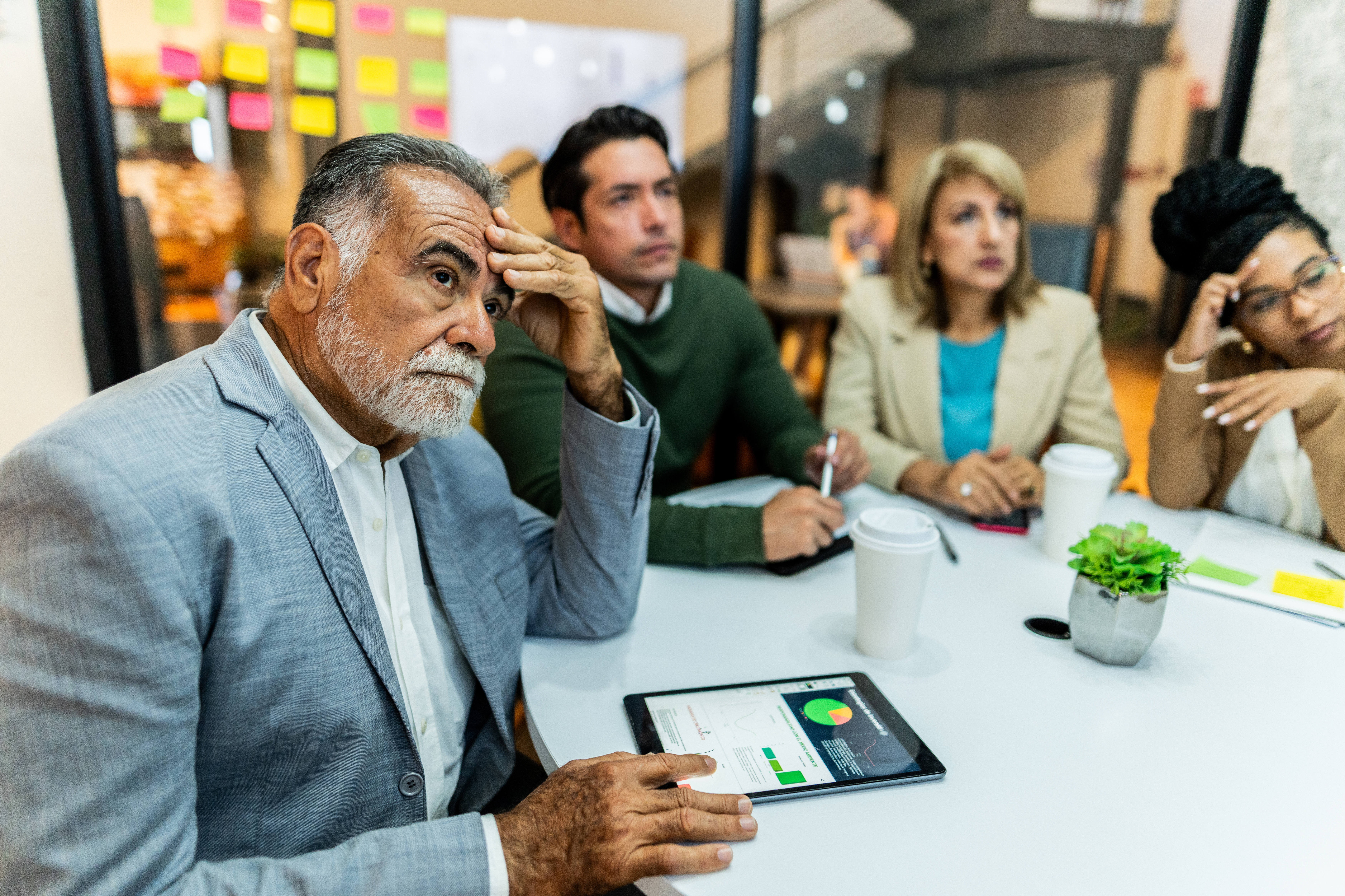 Senior businessman looking concerned during a presentation in a tense office meeting.
