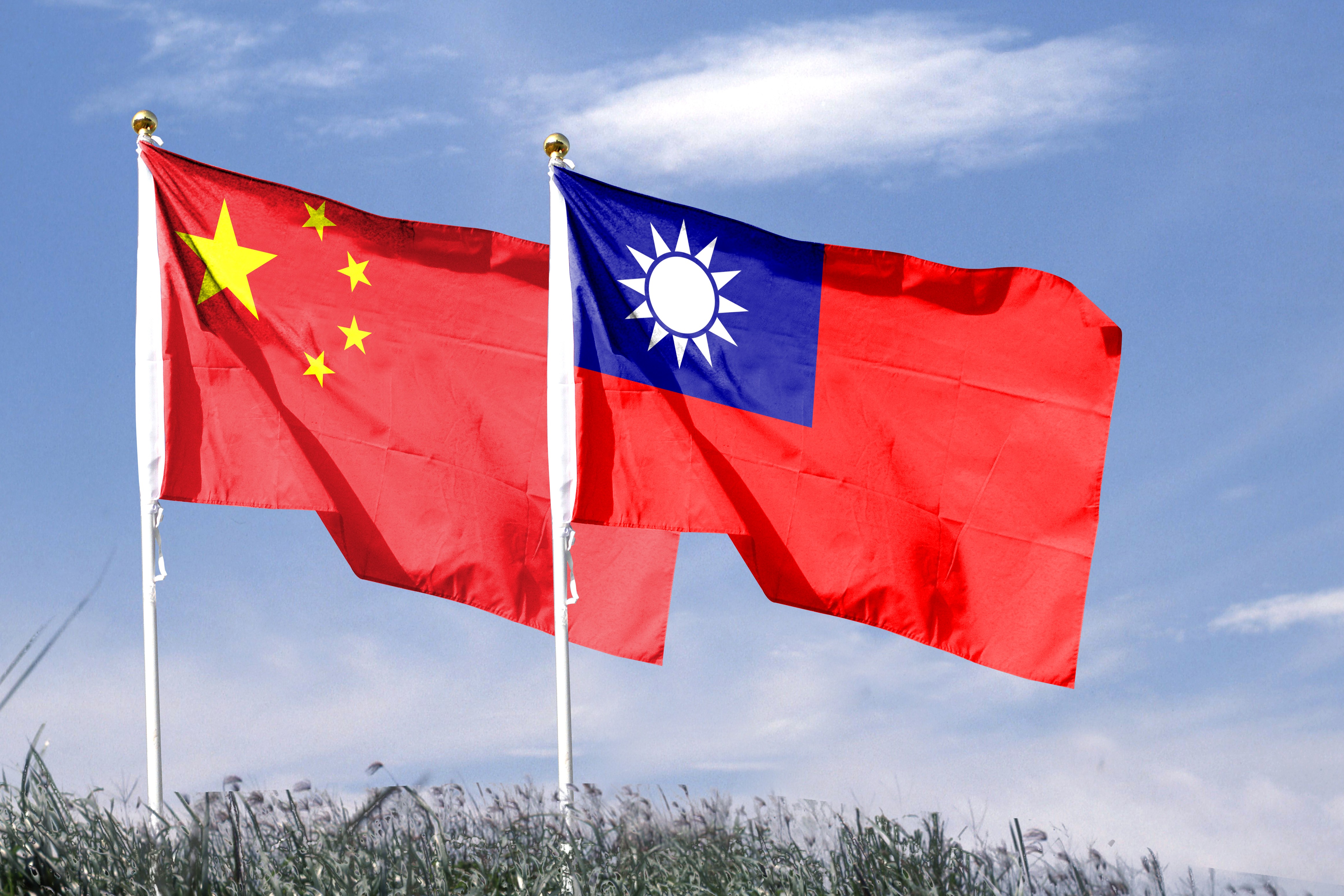 Chinese and Taiwanese flags waving together against a cloudy sky