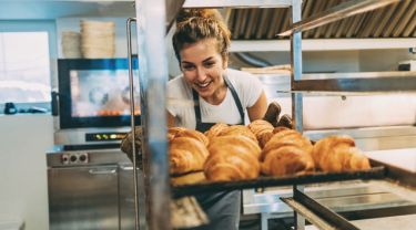 Une personne en tenue de boulanger sort une plaque de croissants dorés d’un four professionnel dans une cuisine de boulangerie.