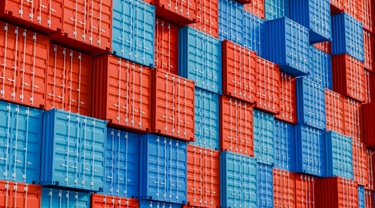 Stack of blue and red cargo shipping containers in terminal yard.