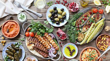 Table extérieure partagée avec brochettes d’agneau méditerranéennes, poulet, légumes rôtis et mezzés.