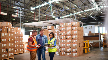 Coworkers discuss orders in a warehouse filled with shipping boxes