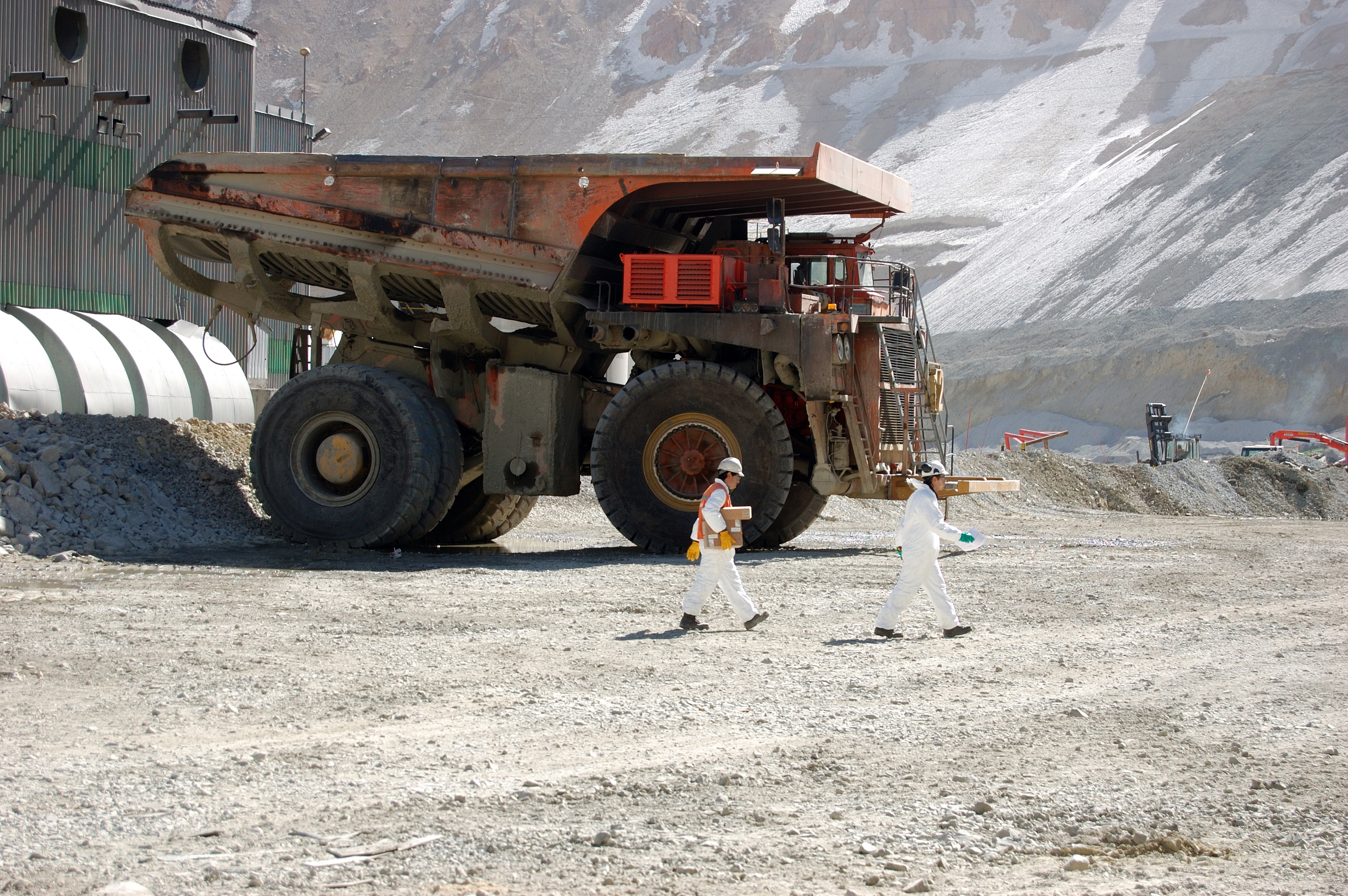 Deux mineurs portant un casque blanc passent devant un gros camion dans une mine de cuivre au Chili.