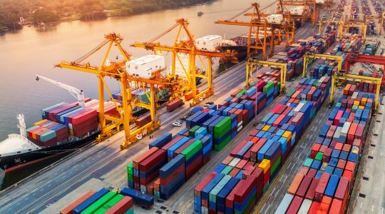 Dans un port d’expédition, au lever du soleil, une file de navires porte-conteneurs avec des grues en marche.