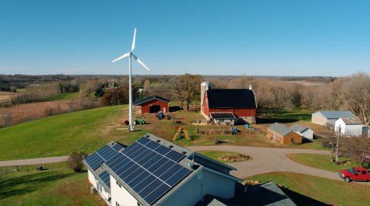 Eocycle’s high-performance wind turbine stands on a rural farm, where solar panels are installed on the farmhouse roof.