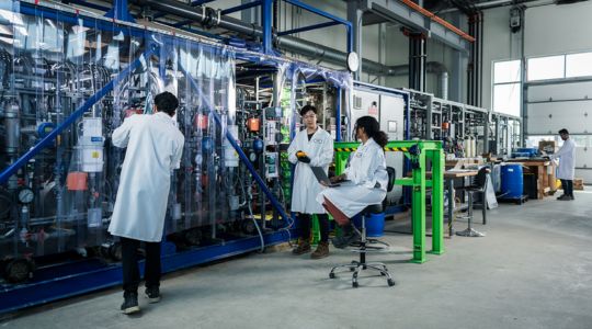 Workers in lab coats stand in front of Mangrove Lithium’s electrochemical equipment used for lithium refinement.