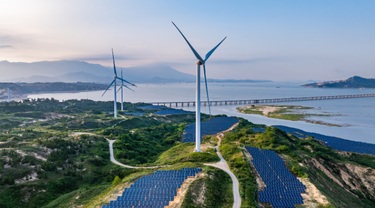 Solar photovoltaic windmill wind energy at sunset alongside ocean.
