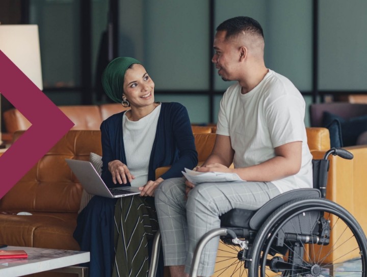 Woman holding a laptop and man in a wheelchair having a conversation in an office