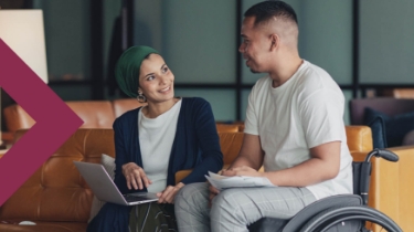 Woman holding a laptop and man in a wheelchair having a conversation in an office