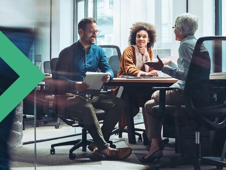Three casually dressed people sitting and talking at a table in an office
