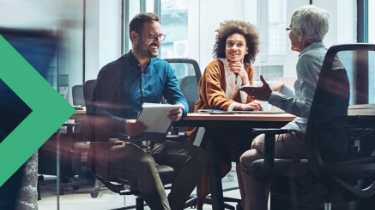 Three casually dressed people sitting and talking at a table in an office