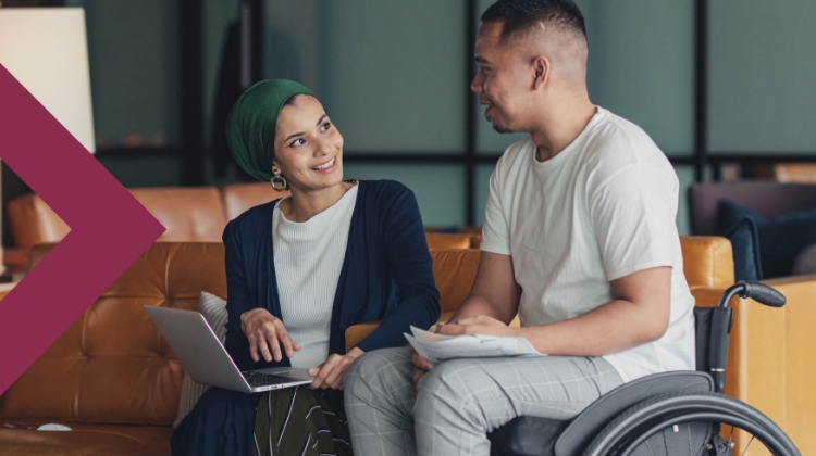 Woman holding a laptop and man in a wheelchair having a conversation in an office