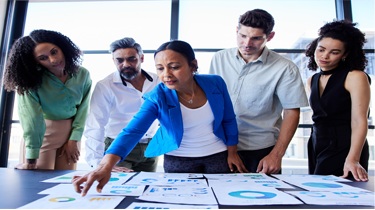 Diverse group of business professionals reviewing economic charts and graphs during a business discussion.