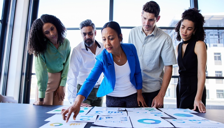 Diverse group of business professionals reviewing economic charts and graphs during a business discussion.