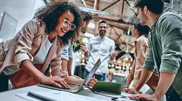 Smiling colleagues gather around table in office.