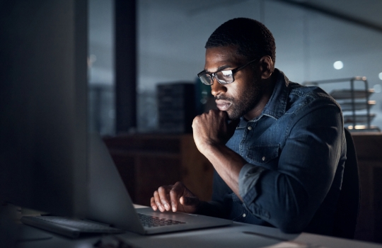 Un jeune homme d'affaires travaillant tard sur un ordinateur portable dans un bureau moderne.