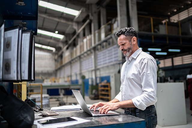 Mature businessman using a laptop in a factory setting.