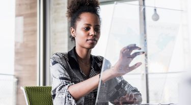 A woman interacting with a transparent touchscreen while typing on a keyboard in an office environment.