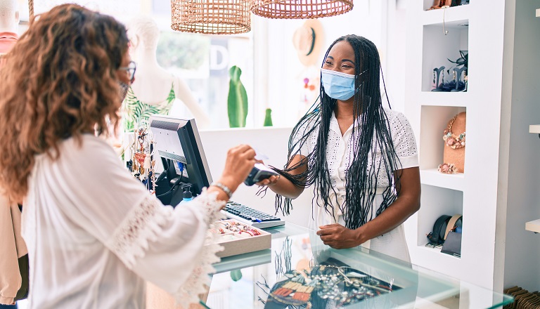 Female shopkeeper wearing face mask serves customer
