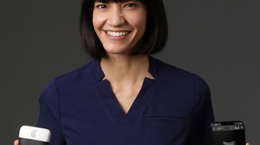 Smiling women holding Clarius portable ultrasound device in left hand and a smartphone in the right hand which shows an image of a fetal ultrasound.