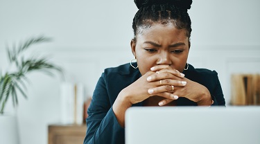 Une femme semble confuse alors qu'elle lit un document sur son ordinateur au bureau.