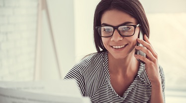 Smiling woman checking her laptop and talking to a customer on her phone 