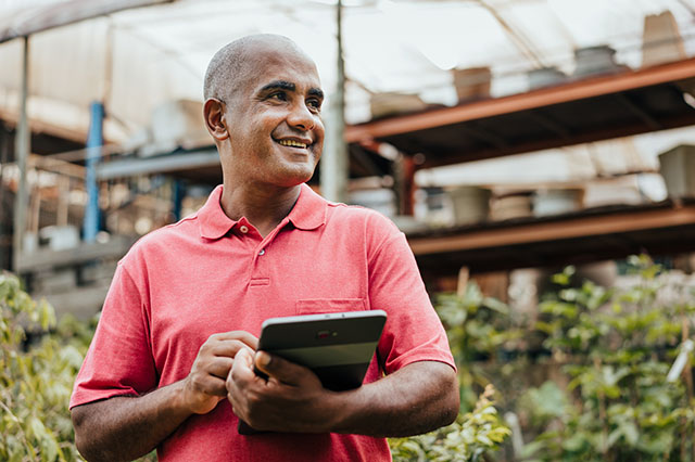 A smiling, mature Hispanic man holding a tablet in a retail shop.