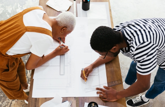 Two architects finalizing a blue print over a drawing table