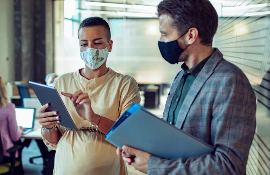 Close up of two business people having a quick chat in the office with face masks on