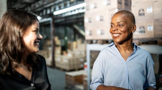 Deux femmes d’affaires marchant et souriant dans un entrepôt.