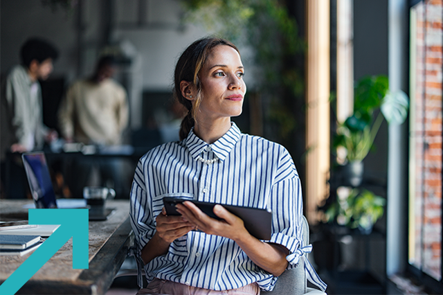 Une femme d'affaires contemplative, équipée d'une tablette numérique, dans un bureau moderne, regarde par la fenêtre.