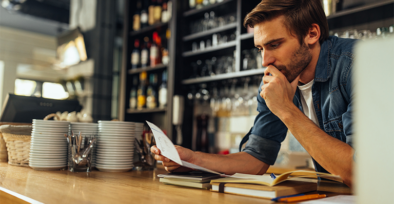 Worried restaurant owner checks business documents while standing behind counter