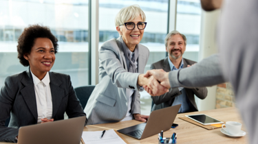 Three individual smiling and facing one other person. One of them is shaking hands with one person.