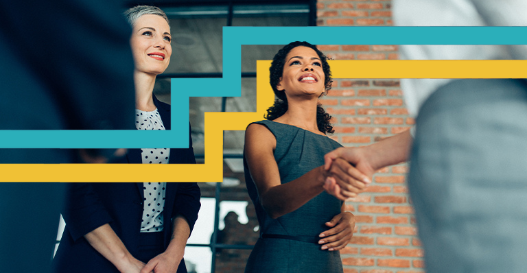 Two women smiling and facing two other people. One of the women is shaking hands with one person.