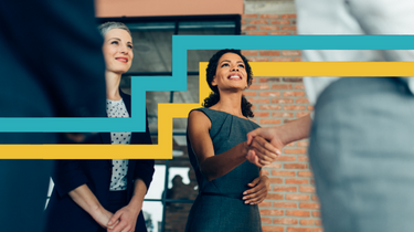 Two women smiling and facing two other people. One of the women is shaking hands with one person.